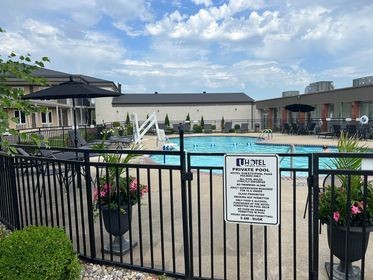 Hotel outdoor swimming pool surrounded by a black fence, with lounge chairs and umbrellas nearby.