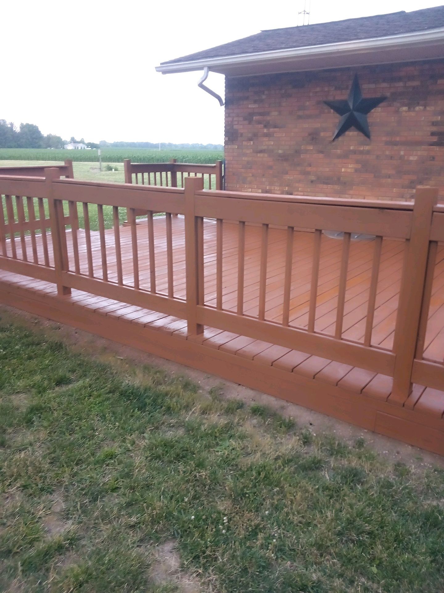 Wooden deck attached to a brick house with a star decoration, overlooking a grassy field.